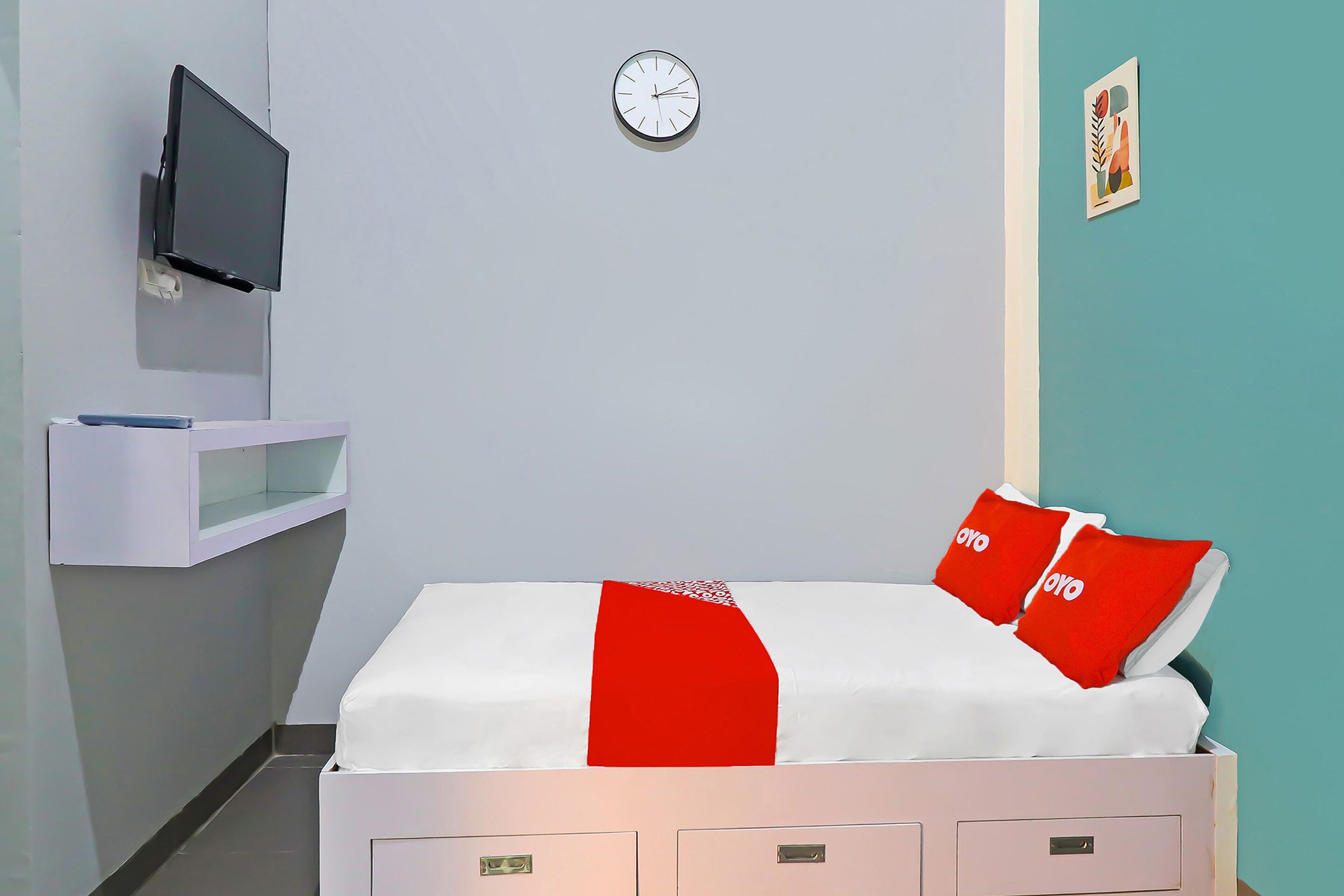 Een hotelkamer met een bed, een aan de muur bevestigde televisie, een klok en een klein plankje met een boek.