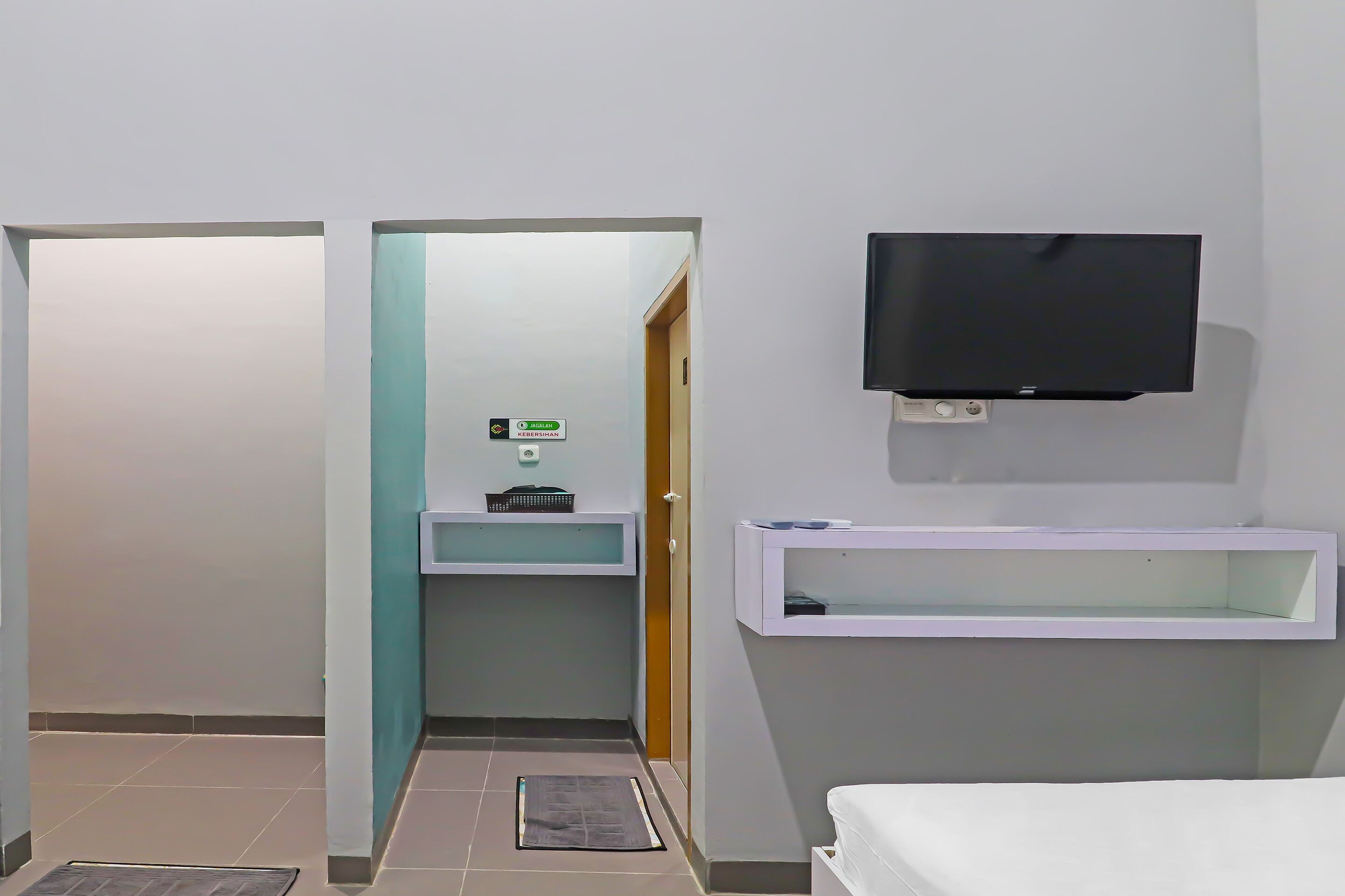 Une chambre d’hôtel avec un lit, un téléviseur fixé au mur, une petite étagère et une porte donnant sur une salle de bain.