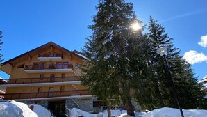 Ein mehrstöckiges Holzgebäude mit Balkonen, umgeben von Schnee und Bäumen, unter blauem Himmel.