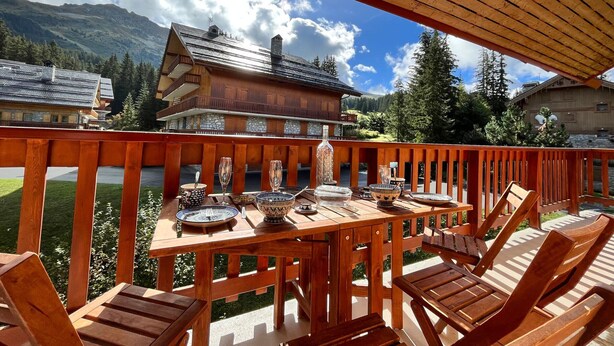 Eine Holzterrasse mit Essplatz, mit Blick auf eine gebirgige Landschaft und traditionelle Holzhäuser.