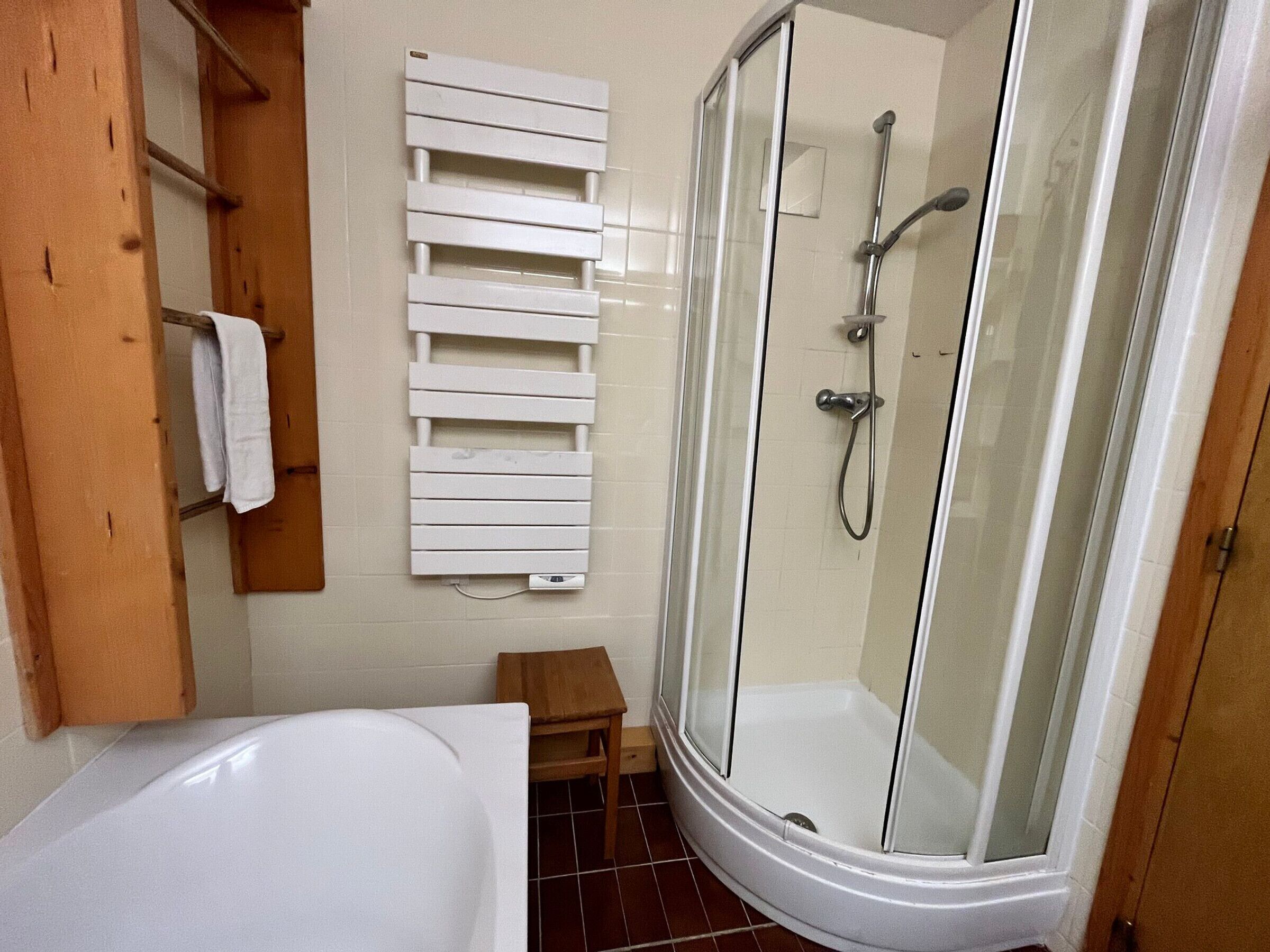 A bathroom with a glass-enclosed shower, a white bathtub, and a towel rack.