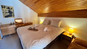 Ein Hotelzimmer mit einem großen Bett, einem Holzkopfteil, einem Nachttisch mit Lampe, einem Schreibtisch mit Stuhl und einem Bild an der Wand.