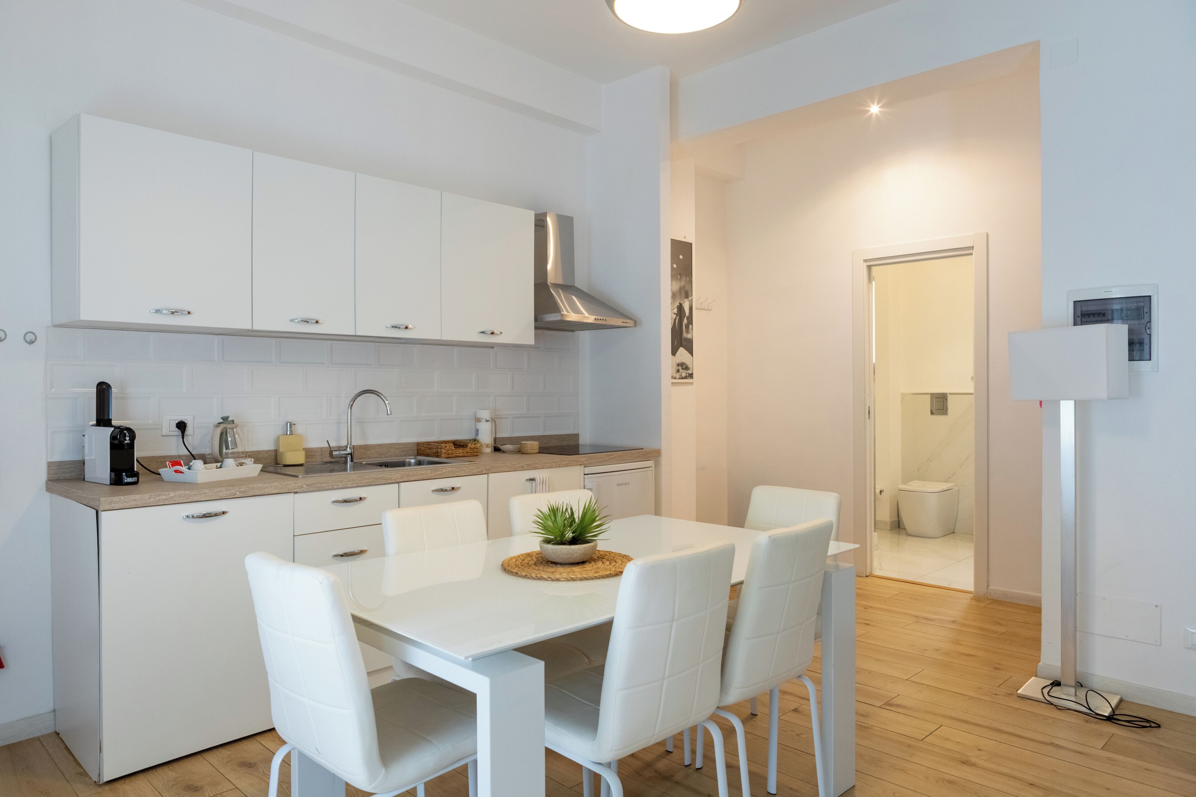 A modern kitchen with white cabinetry, a central island with chairs, and a dining table.