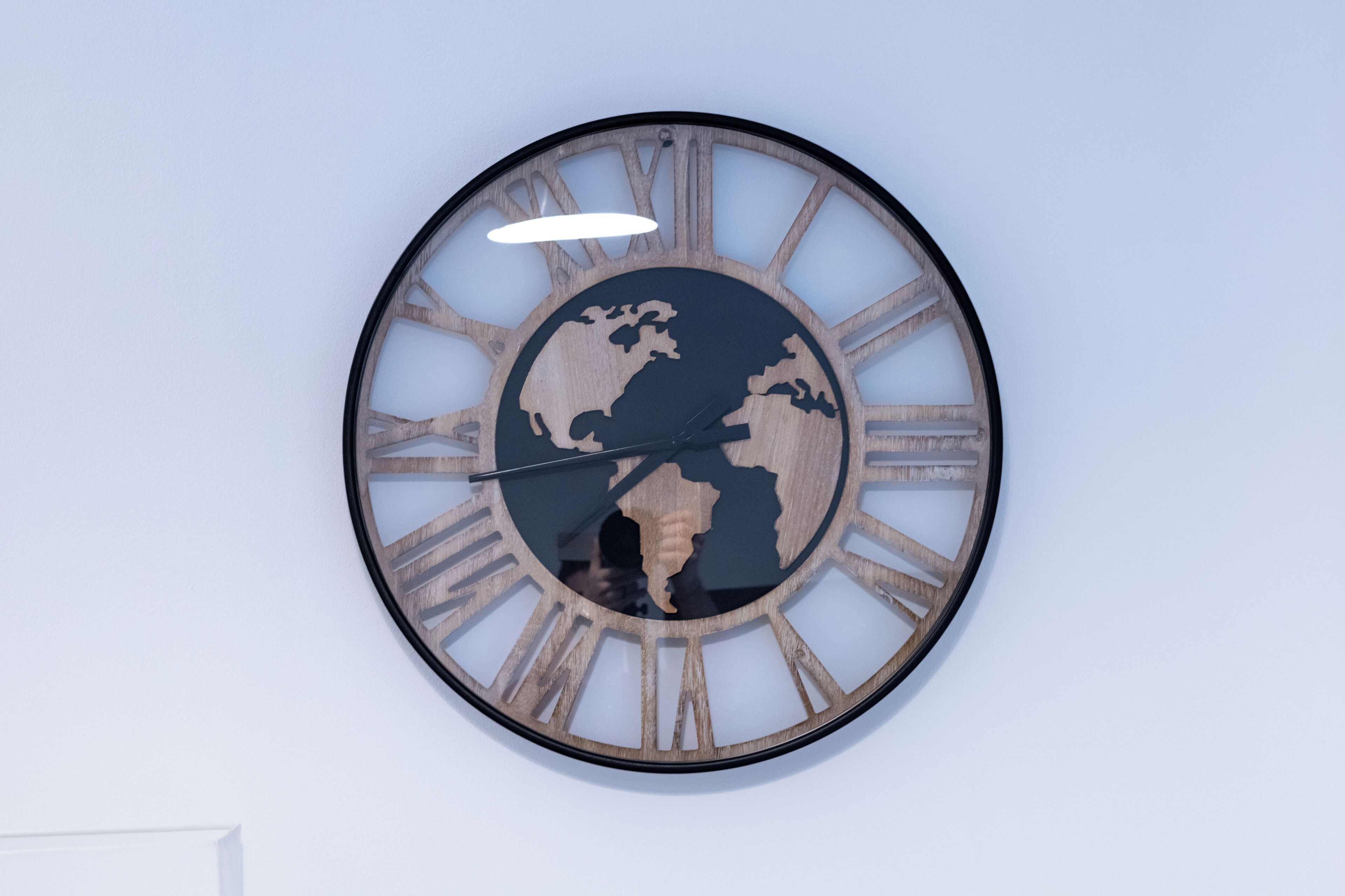 Een ronde wandklok met houten lijst en Romeinse cijfers, met een wereldkaart in het midden.
