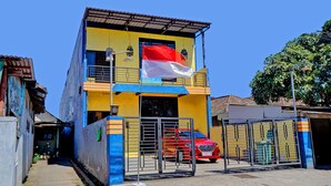 A two-story building with a flag, a red car parked in front, and a gated entrance. - OYO Life 92915 Duta Amnan Syariah (Sidoarjo)