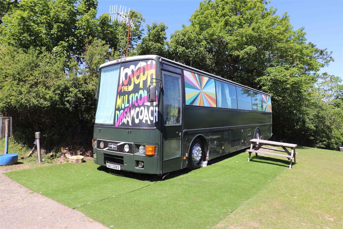 A bus with colorful graphics and text on its side and back, parked on a grassy area with a picnic table nearby.