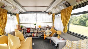 A cozy interior with a sofa, armchair, and a small table with a lamp. A bookshelf filled with books is in the background. - Fosfelle Glamping (Bideford)