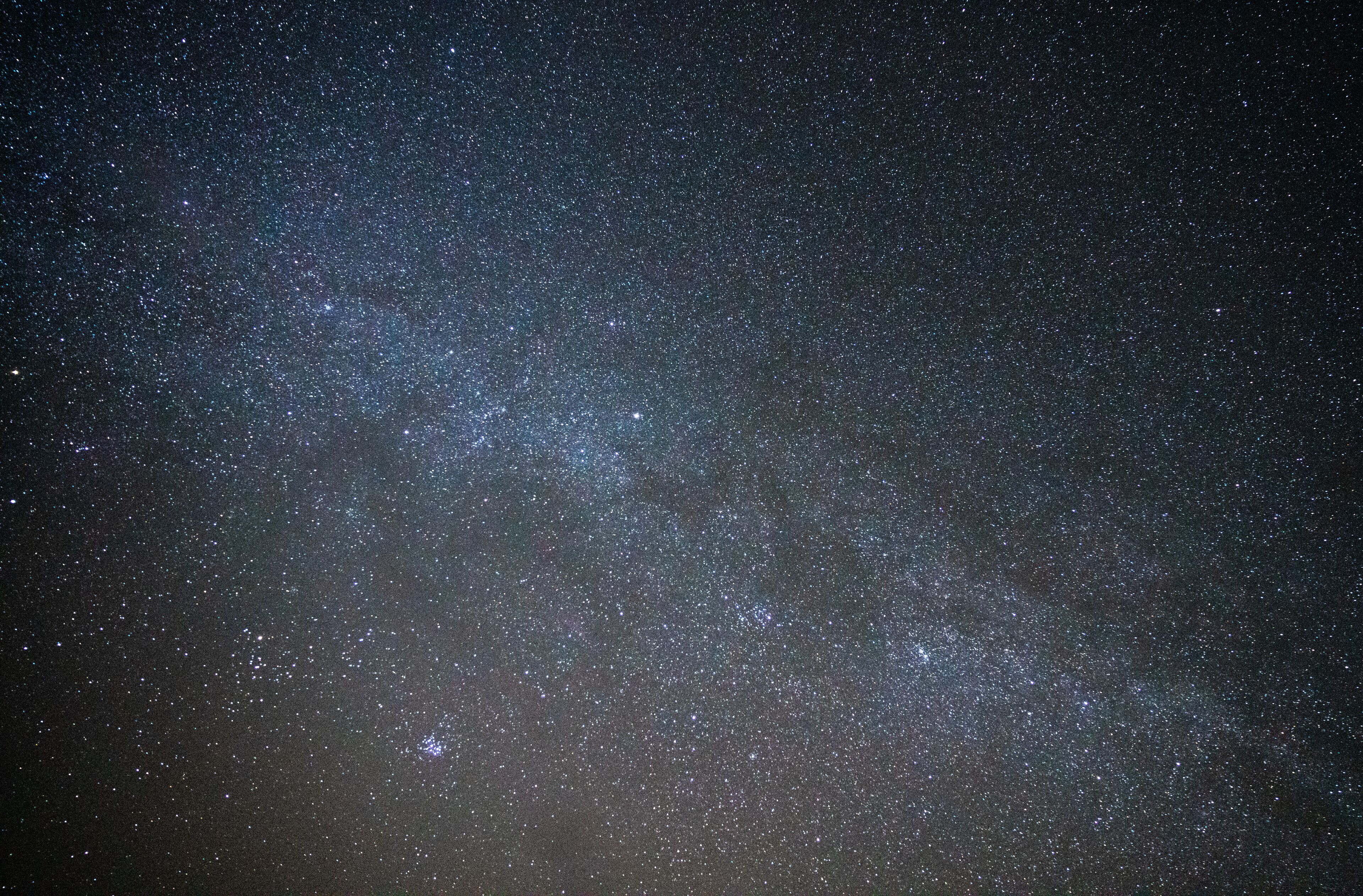 A starry night sky with a dense cluster of stars and a faintly visible galaxy.