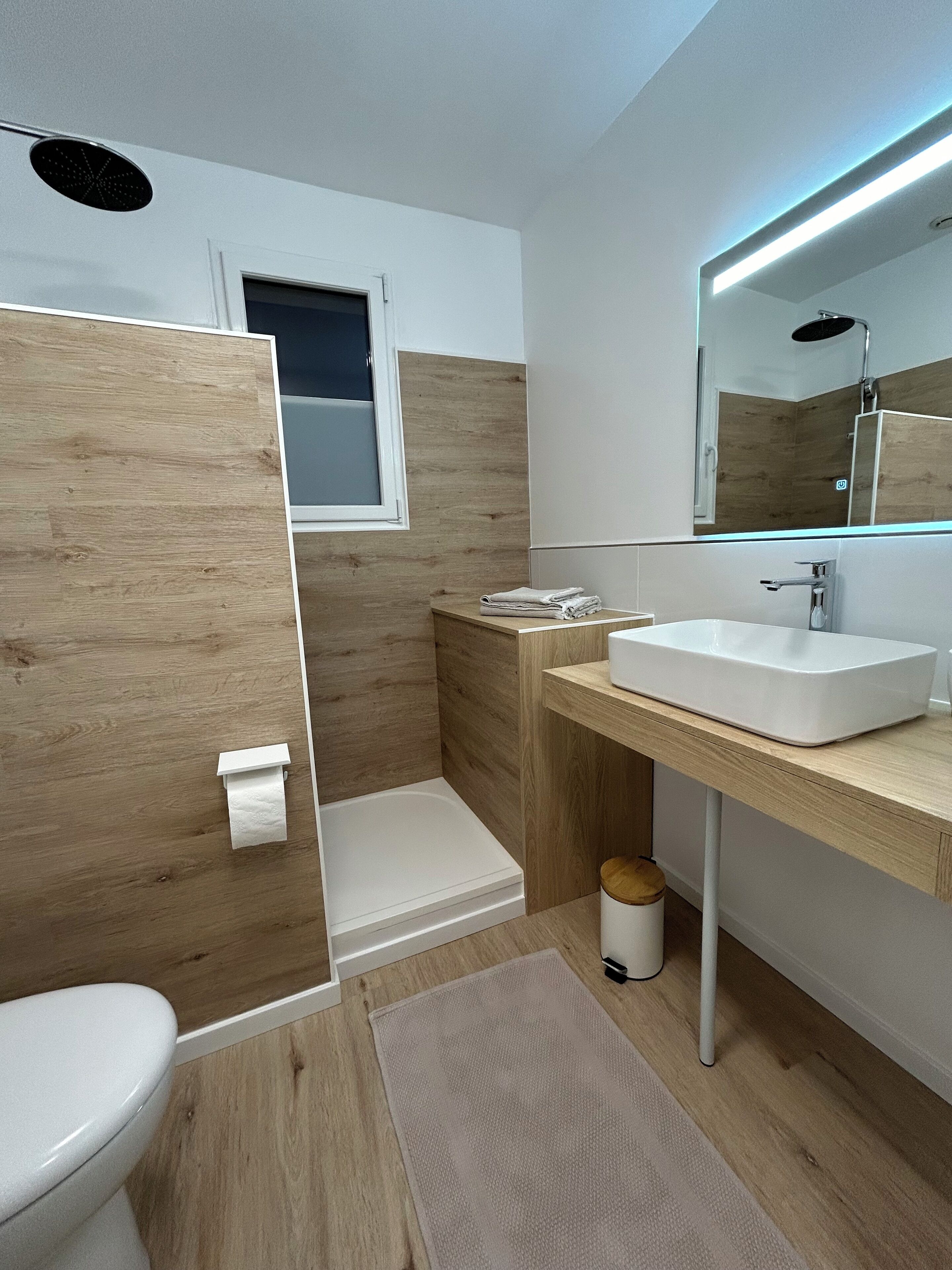 A modern bathroom with a wooden vanity, a white sink, a mirror, and a shower.