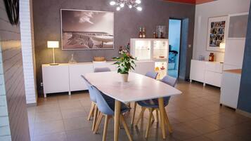 A modern dining area with a white table, blue chairs, and a potted plant.
