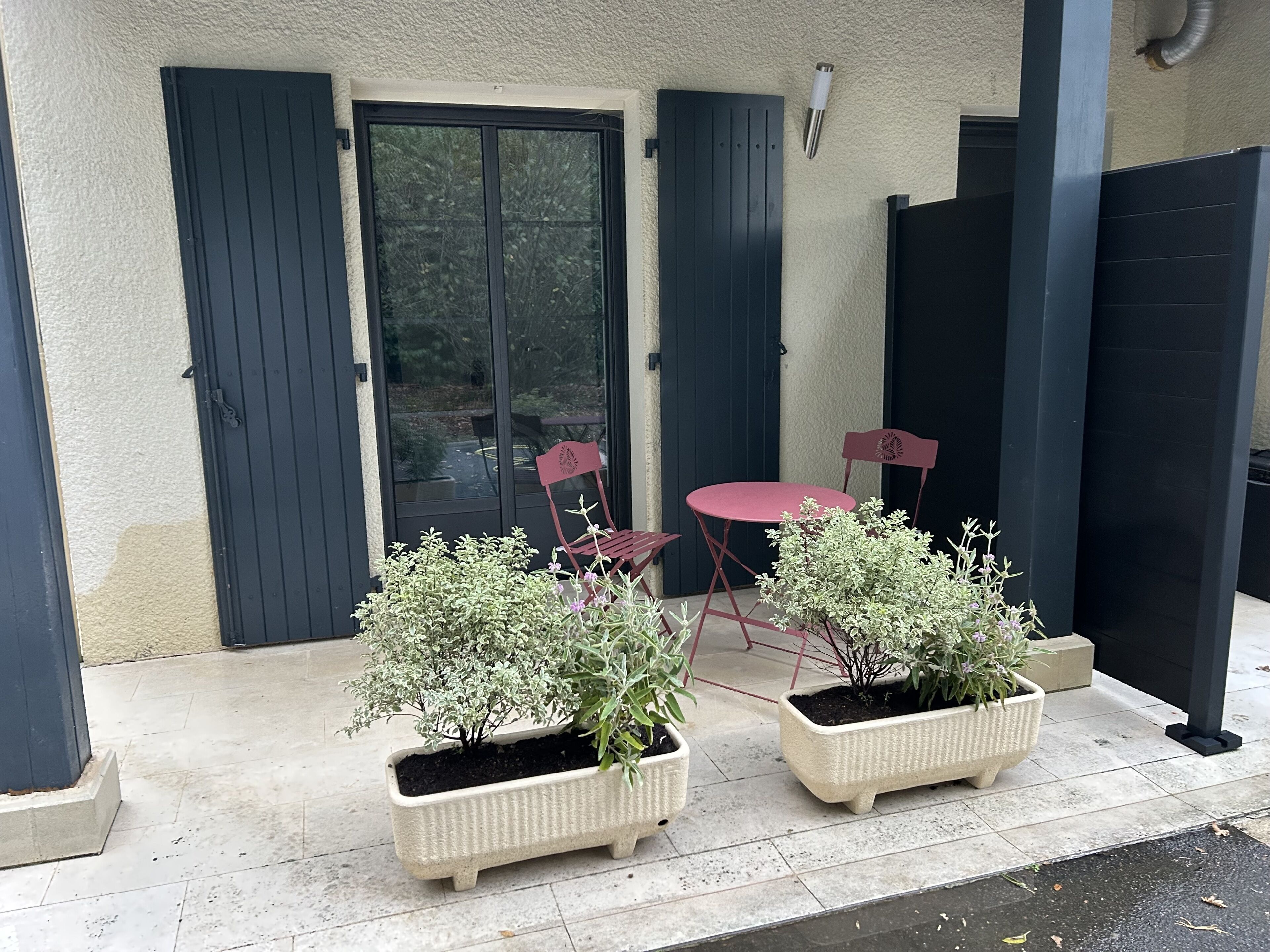 Un patio con mesa y sillas, plantas en macetas y un gran ventanal corredera.