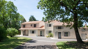 A two-story building with a tiled roof, a paved driveway, and surrounding greenery.