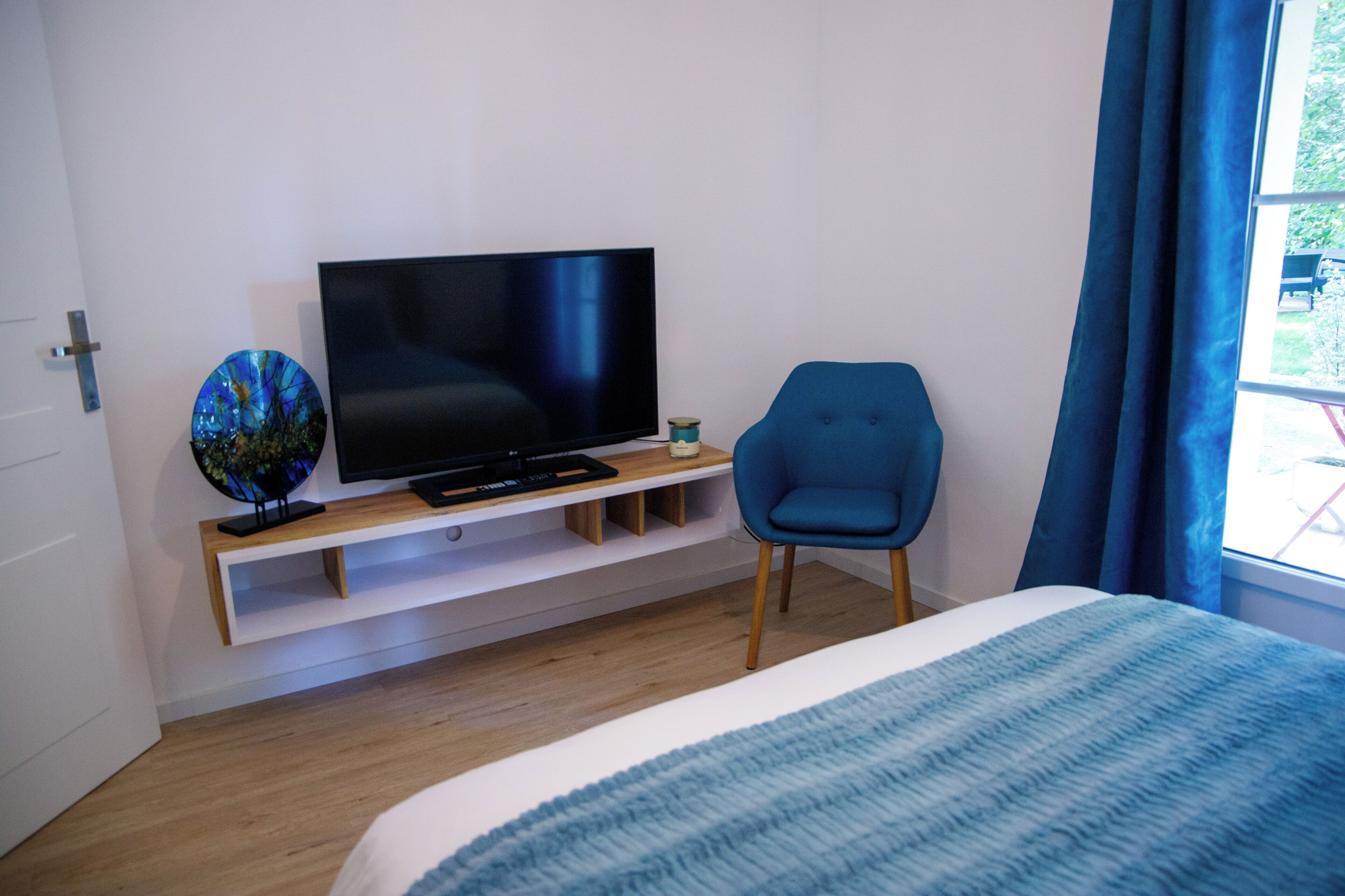 Quarto de hotel moderno com uma cama grande, uma televisão de tela plana em um suporte de madeira, uma poltrona azul e um globo decorativo pequeno.