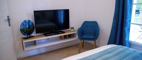 Quarto de hotel moderno com uma cama grande, uma televisão de tela plana em um suporte de madeira, uma poltrona azul e um globo decorativo pequeno.