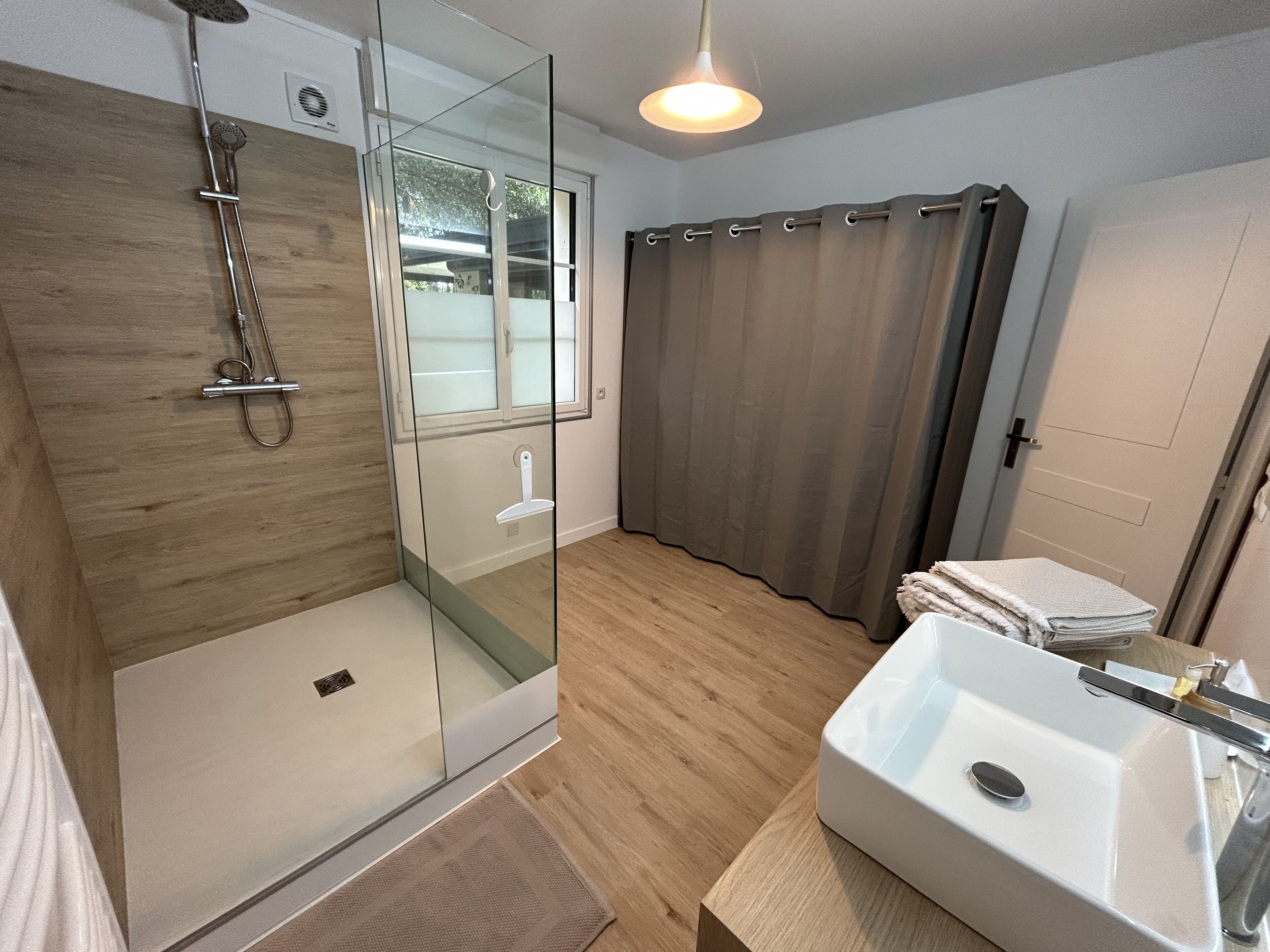 A modern bathroom with a glass-enclosed shower, a white sink, and a wooden floor.