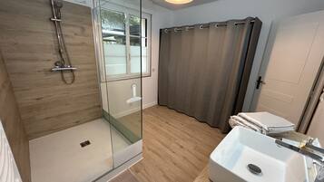 Un baño moderno con ducha acristalada, lavamanos blanco y suelo de madera.