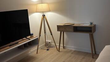 A hotel room with a wooden floor, a TV on a wooden stand, a desk with a lamp, and a bed.