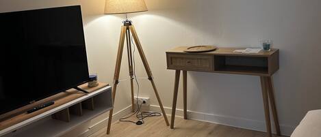 Habitación de hotel con piso de madera, televisor sobre un mueble de madera, escritorio con lámpara y una cama.