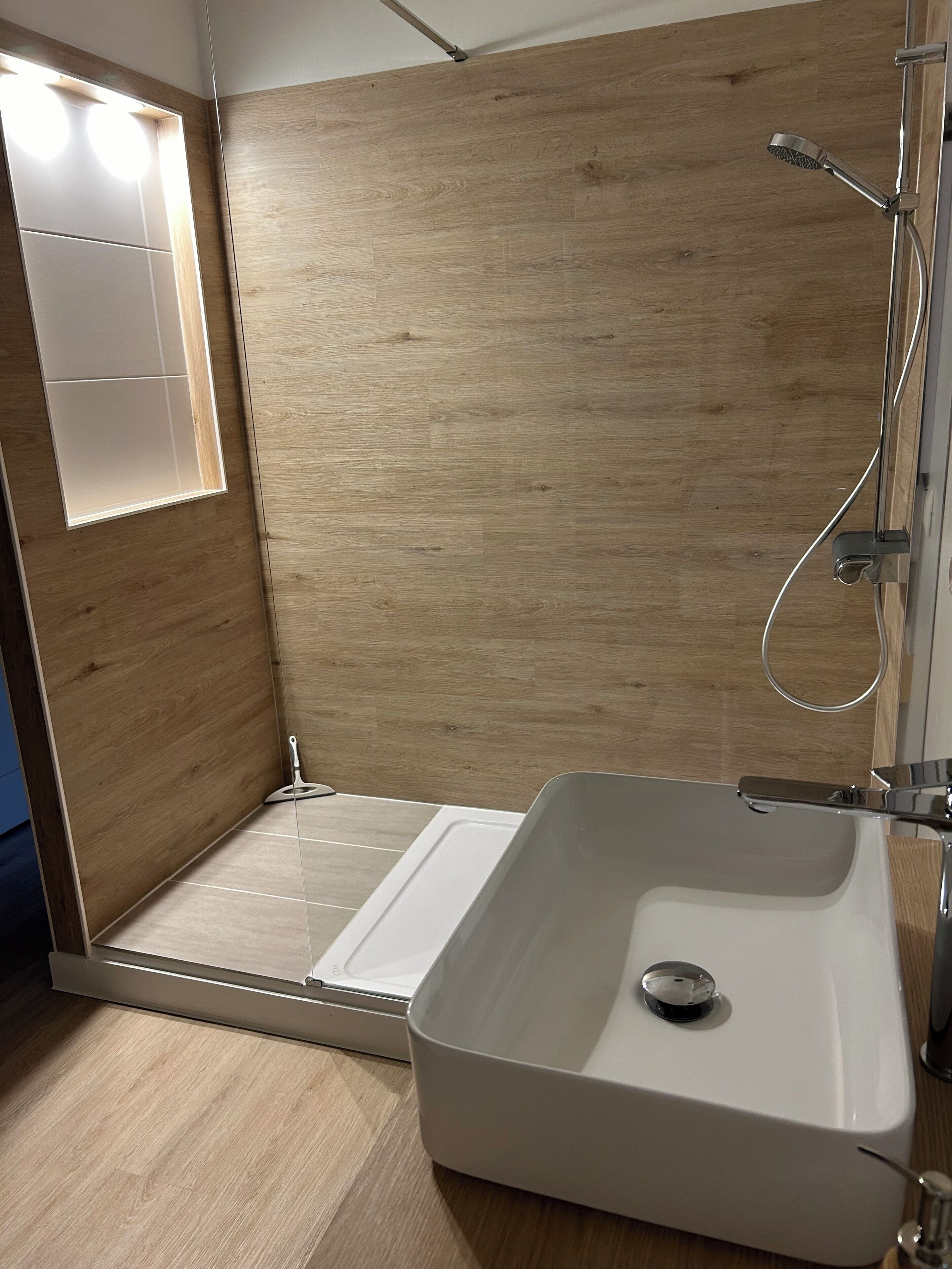 Ein modernes Badezimmer mit Holzboden, einem weißen Waschbecken und einer Duschkabine.
