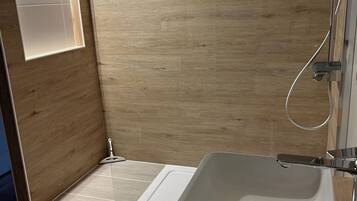 Ein modernes Badezimmer mit Holzboden, einem weißen Waschbecken und einer Duschkabine.