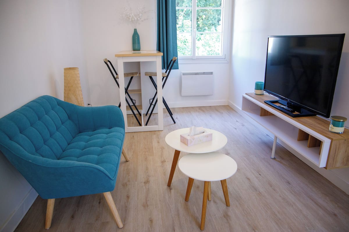 Ein modernes Wohnzimmer mit einem blauen Sofa, einem Flachbildfernseher und einem kleinen weißen Tisch.