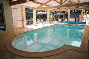 Piscina coberta com espreguiçadeiras e guarda-sóis, cercada por um deck de madeira e uma parede de tijolos.