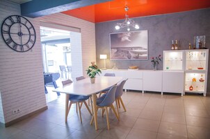 Uma cozinha moderna com bancada branca, um relógio e uma área de refeições com mesa e cadeiras.