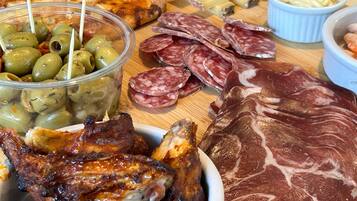 Diversos tipos de carne como salami en rodajas, embutidos y pollo a la parrilla, junto con aceitunas y queso sobre una tabla de madera.