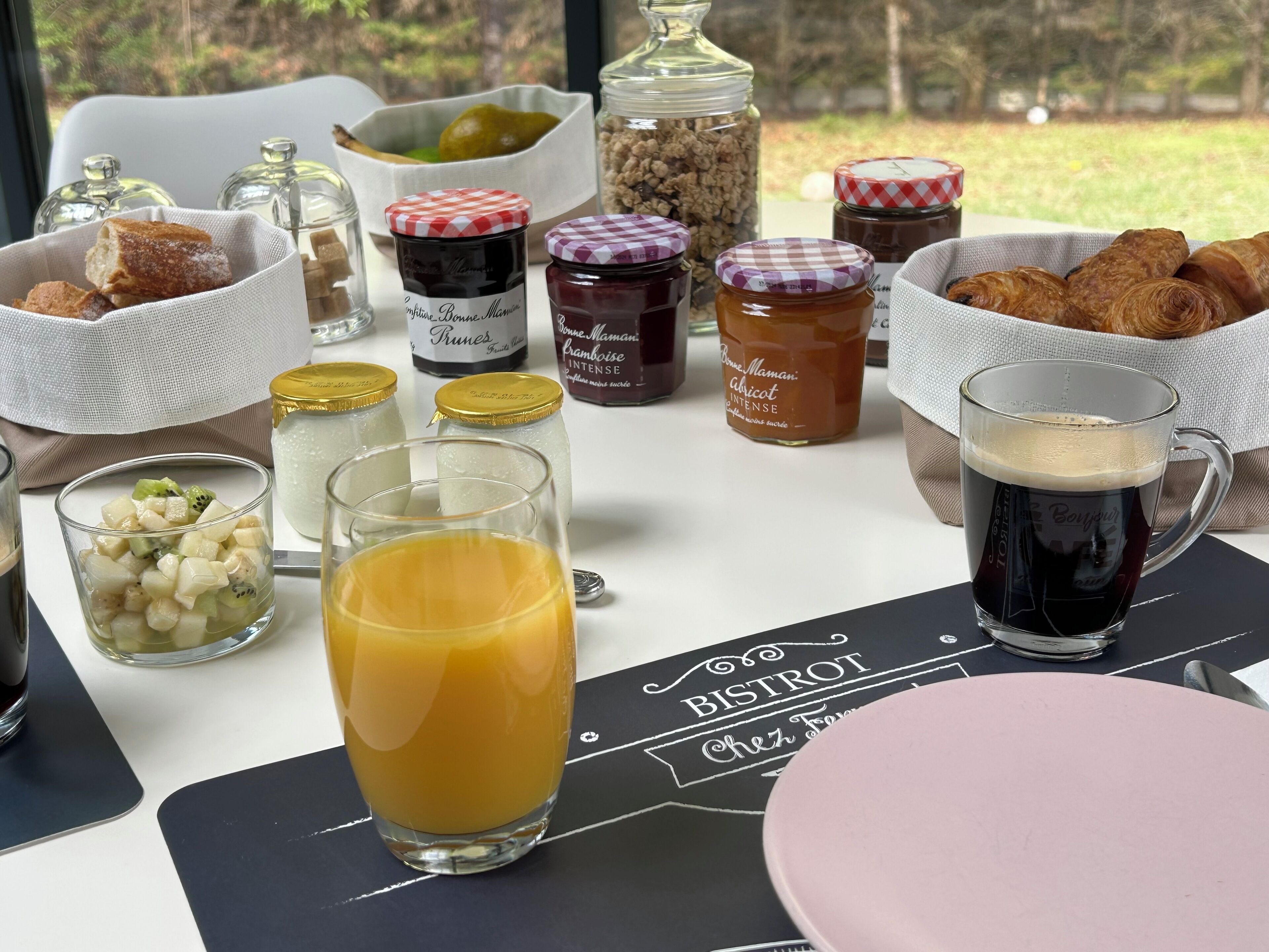 Una mesa de desayuno con diversas opciones de comida, como croissants, fruta y bebidas.