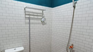 A small bathroom with white tiled walls, a white toilet, a shower with a hose, a metal shelf, and a bucket. - OYO Life  92977 Neba Kost Aesthetic (Tangerang)