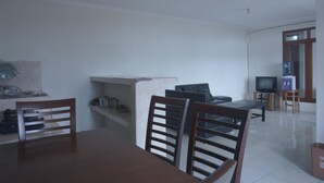 A dining area with a table and chairs, a television, and a small shelf with items. - OYO Life  92977 Neba Kost Aesthetic (Tangerang)