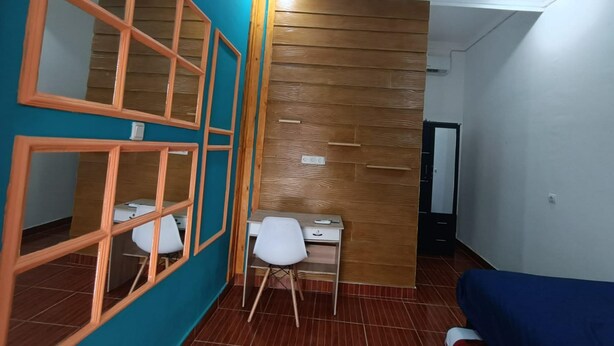A room with teal walls, wooden paneling, a desk with a chair, and a blue sofa. - OYO Life  92977 Neba Kost Aesthetic (Tangerang)