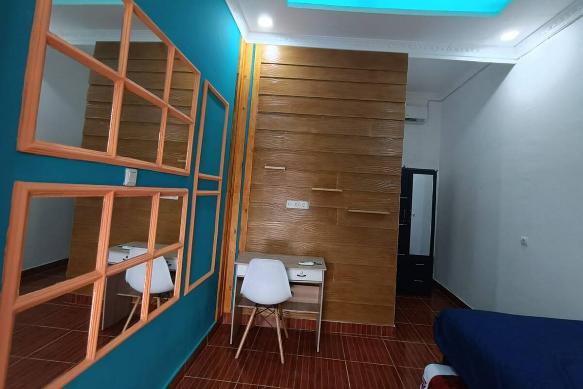Una habitación con paredes azul verdoso, paneles de madera, un escritorio con una silla y un sofá azul.