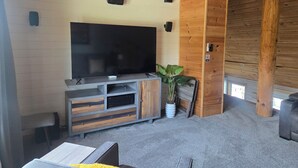 Une pièce dotée d’un grand téléviseur à écran plat, de murs en bois, d’une armoire encastrée en bois, d’une plante en pot et d’une porte sur laquelle est apposé un panneau « défense de fumer ».