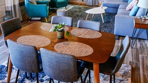 L’intérieur d’un chalet accueillant, avec un plafond en bois, une table à manger entourée de chaises, un canapé et une petite table d’appoint.