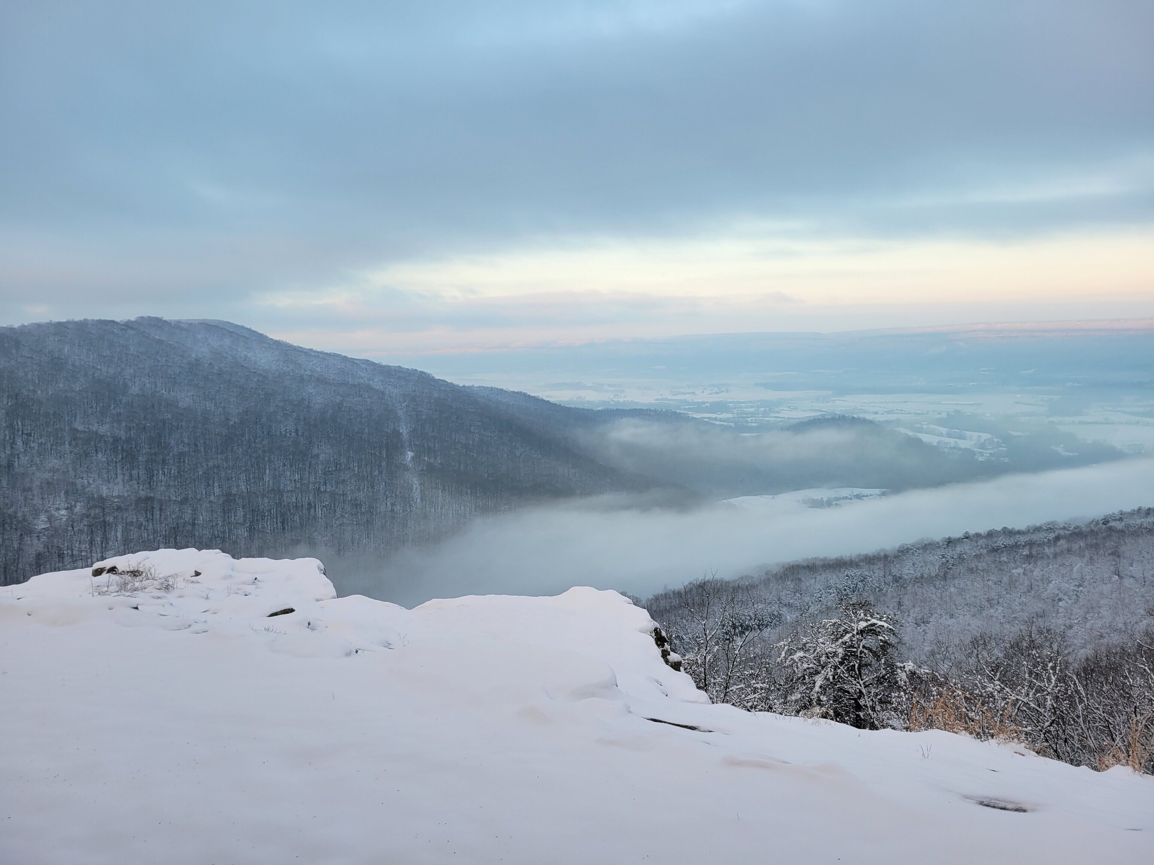 Eine verschneite Berglandschaft mit einem Tal und bewaldetem Gebiet.