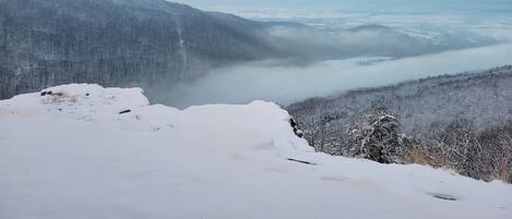 Eine verschneite Berglandschaft mit einem Tal und bewaldetem Gebiet.