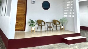 A covered outdoor seating area with a wooden door, two chairs, and potted plants. - Chanmuang Resort   (Phetchaburi)