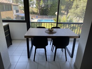 Un comedor con mesa y sillas, vistas a una piscina y un balcón con barandilla.