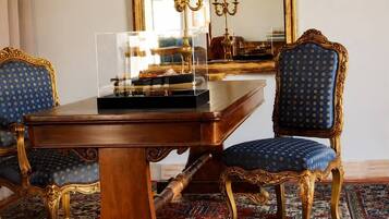 A room with a large ornate mirror, a wooden table, two blue upholstered chairs, and a patterned carpet.