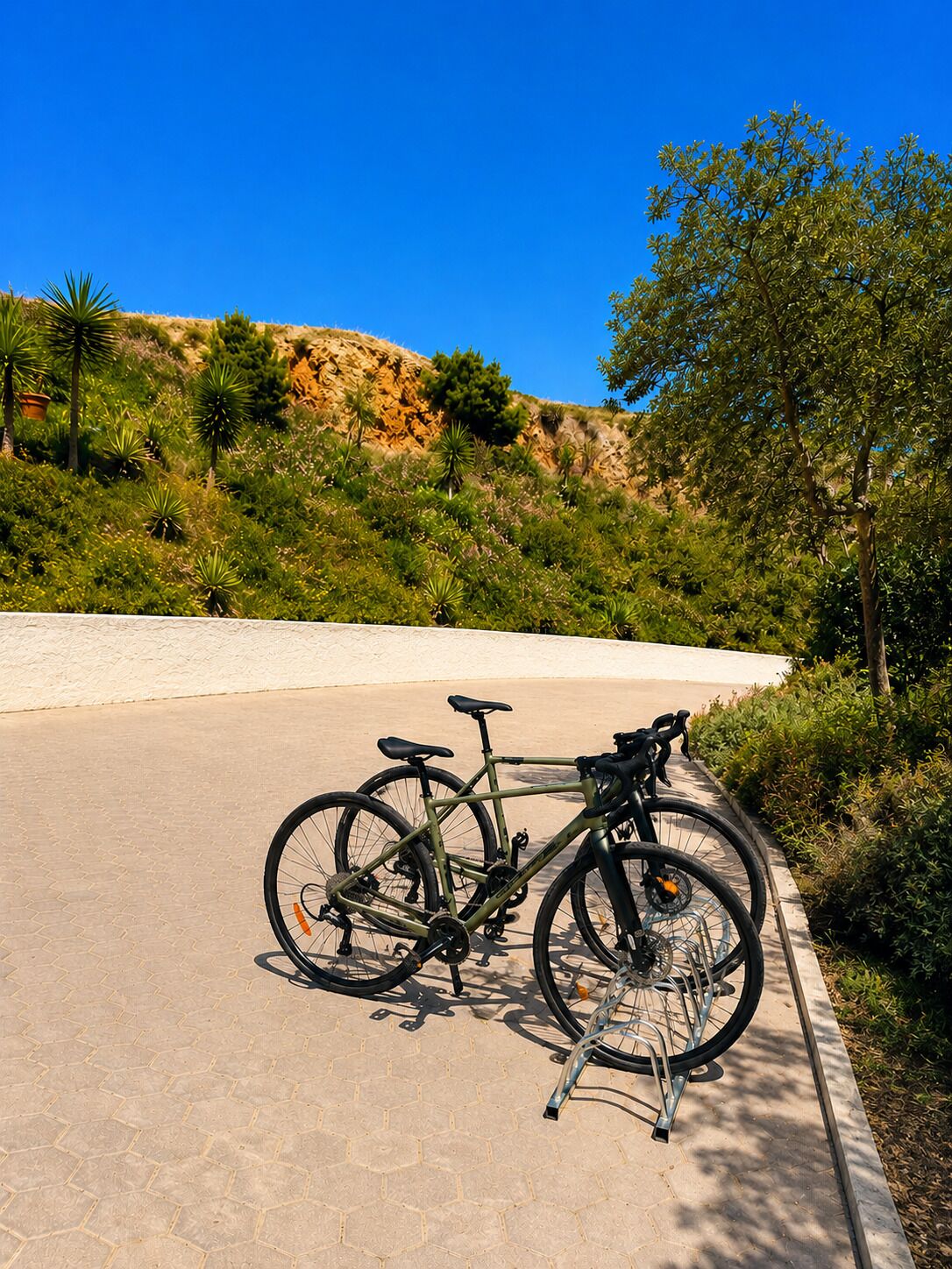 Una bicicletta parcheggiata su una superficie pavimentata, con un cielo azzurro limpido e un paesaggio collinare sullo sfondo.