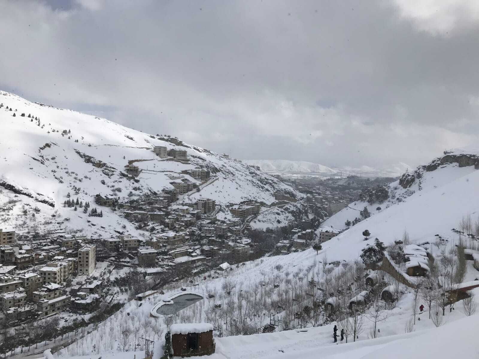 A snow-covered mountainous area with buildings and a small lake.
