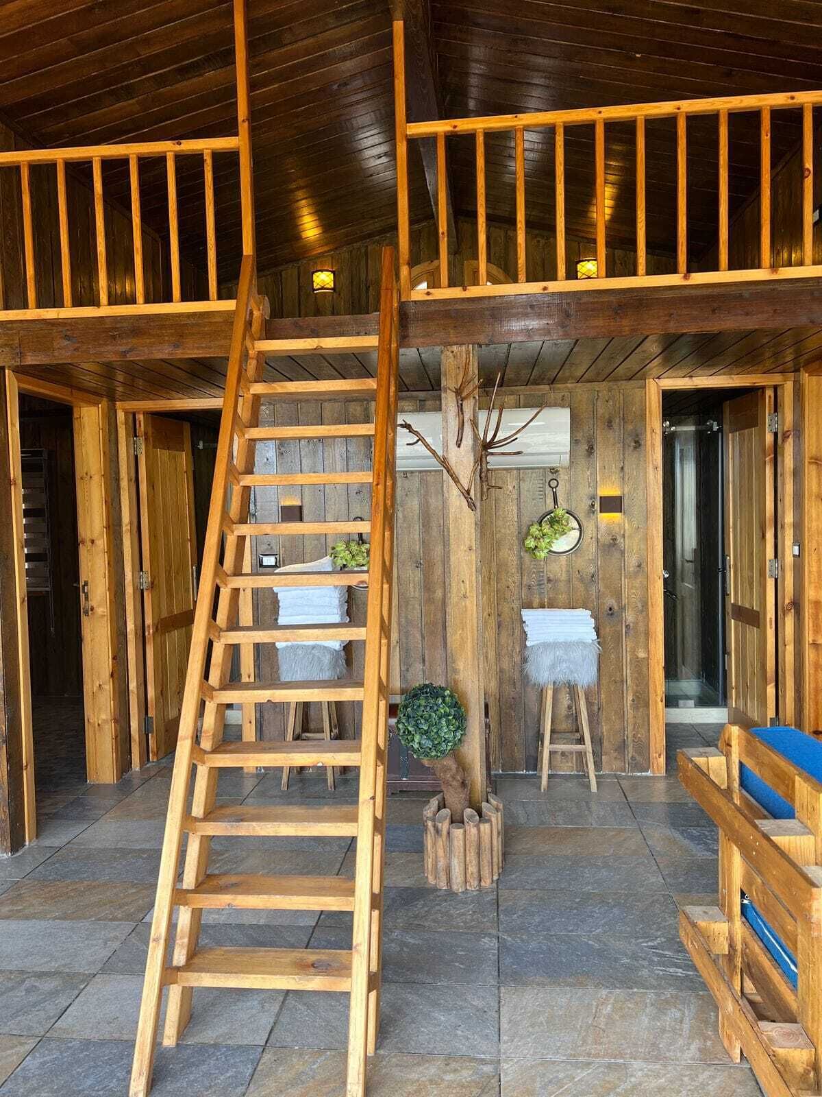 A wooden interior with a central wooden ladder, a small tree, and a bench.