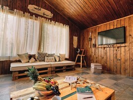 Un acogedor interior de cabaña con techo de madera, un sofá con cojines, un televisor y una mesa con frutas y un cuaderno.