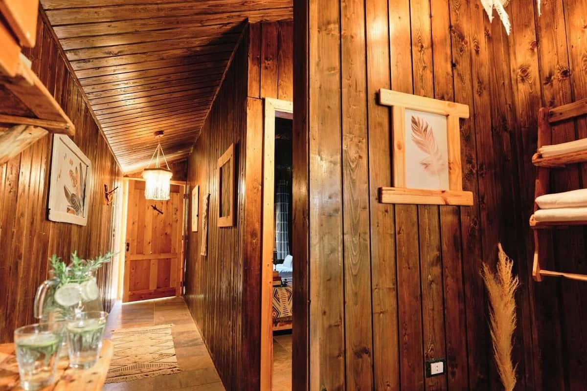 Un couloir en bois, avec une table dressée où sont disposés des verres et une carafe, un tableau encadré accroché au mur et une porte donnant sur une autre pièce.