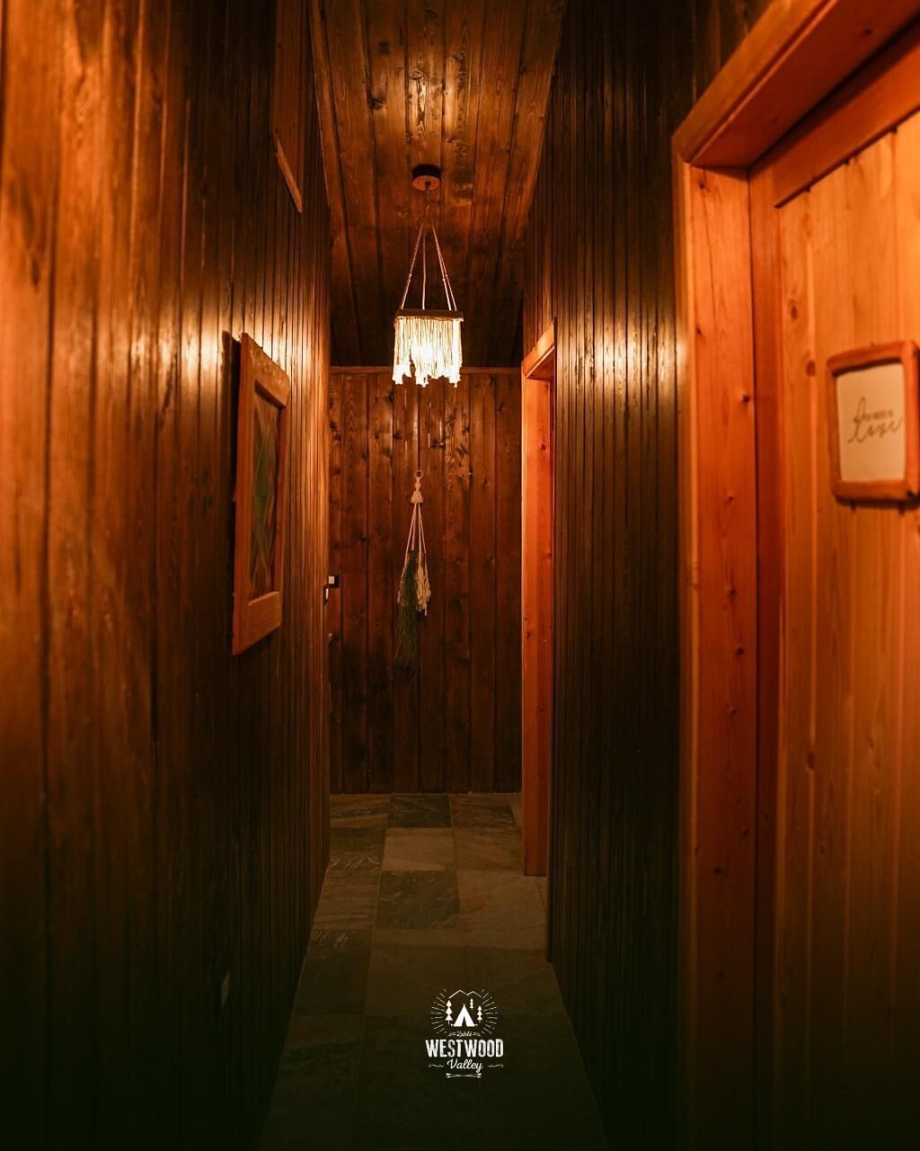 A wooden hallway with a chandelier, a checkered floor, and a sign on the right wall.
