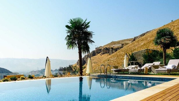 Une piscine avec une terrasse en bois, des chaises longues et des palmiers.
