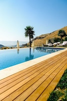 Piscina con terraza de madera, sillas de descanso y palmeras.