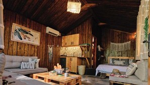 L’intérieur d’un chalet rustique, avec des murs en bois, un plafond en bois, un canapé, un lit, une table basse et un luminaire suspendu.