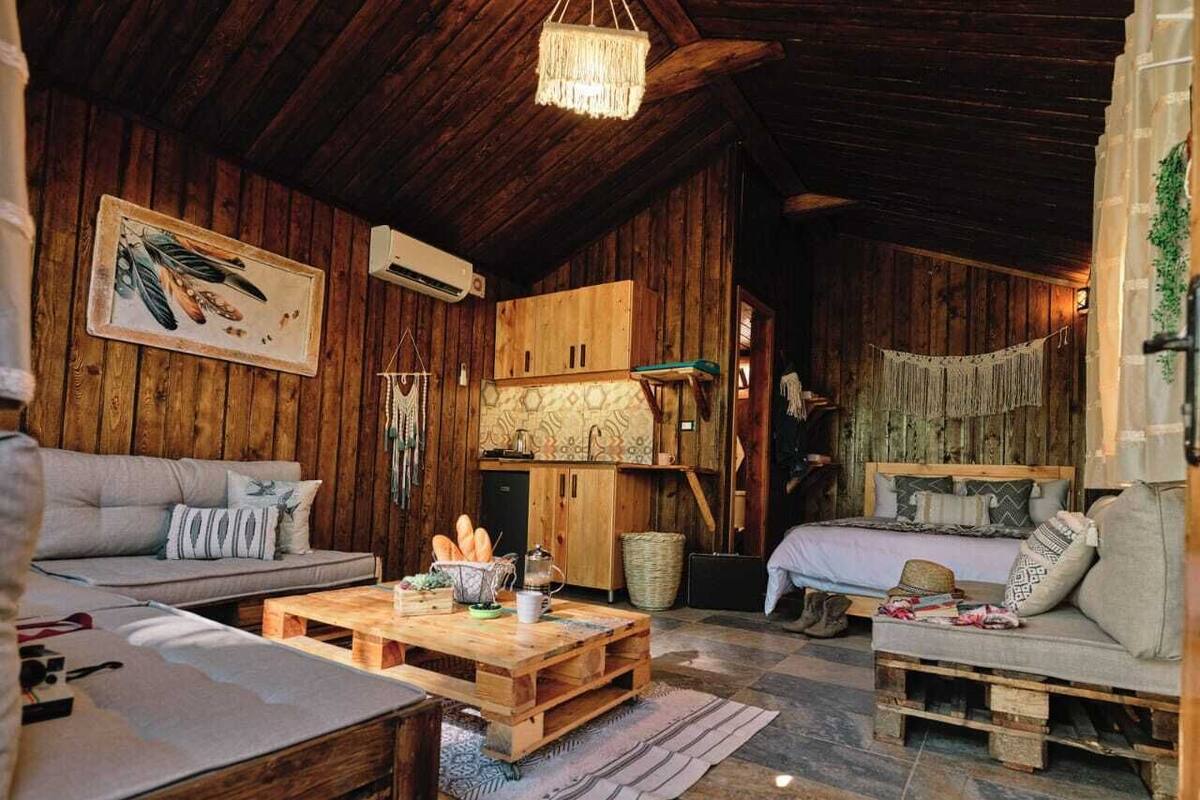 L’intérieur d’un chalet rustique, avec des murs en bois, un plafond en bois, un canapé, un lit, une table basse et un luminaire suspendu.
